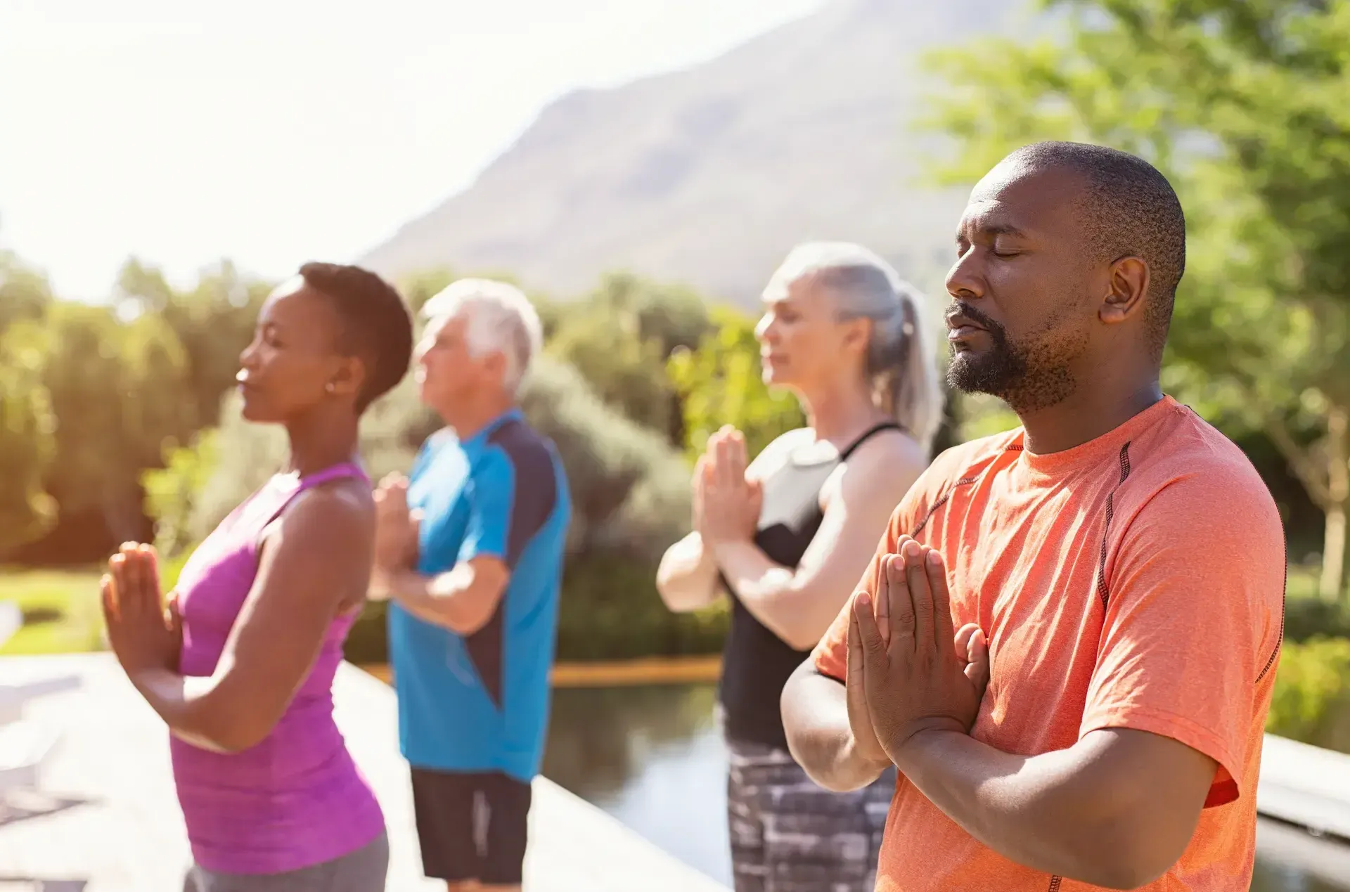 Mature adults standing with hands at their hearts, eyes closed, outdoors in the sun