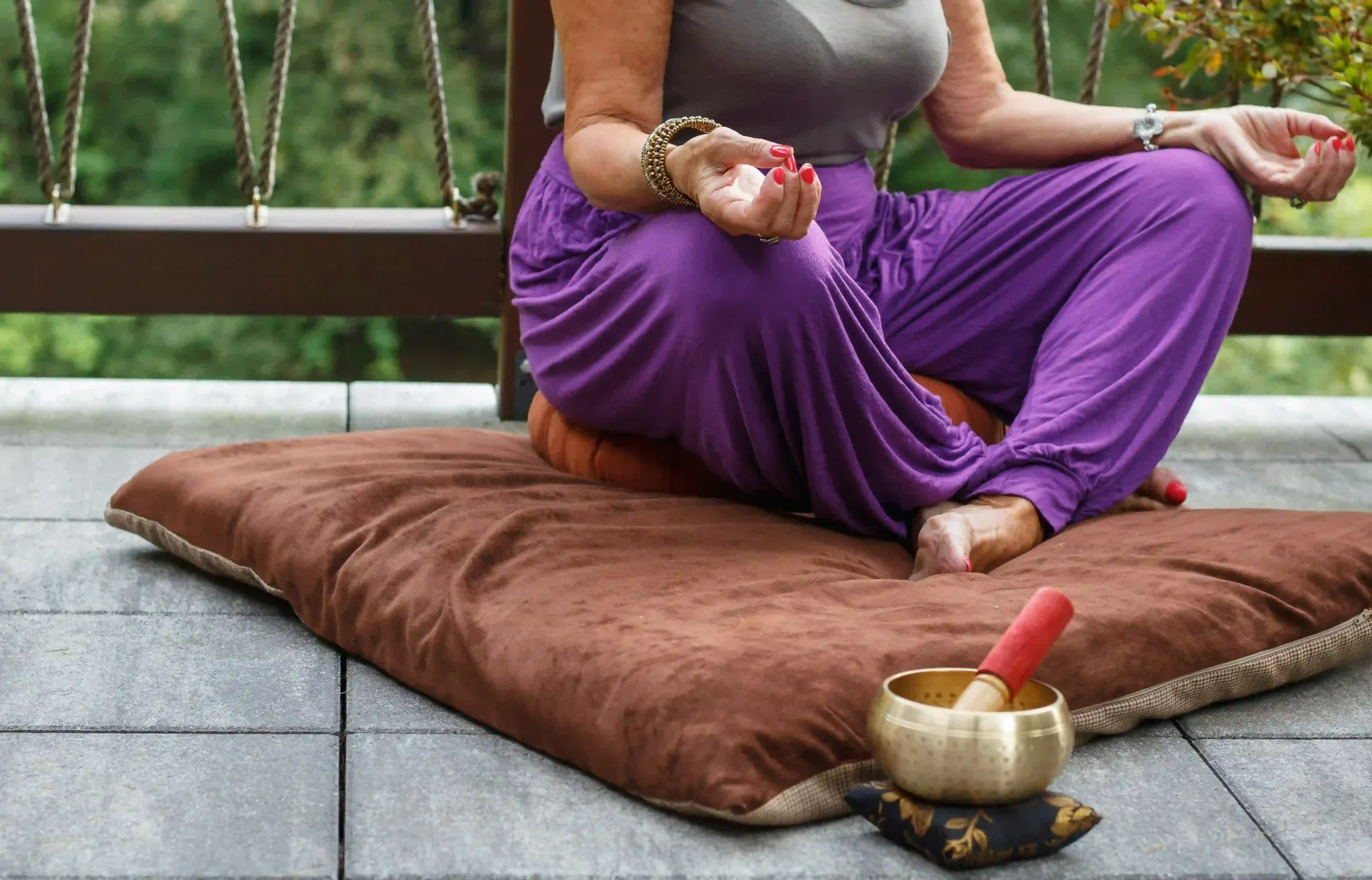 A woman seated on a floor cushion in meditation beside a singing bowl